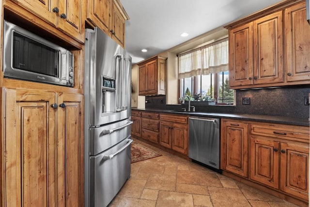 40924 Purple Sage St, Steamboat Springs, CO 80487 - kitchen with stainless steel appliances, a sink, brown cabinets, dark countertops, and tasteful backsplash