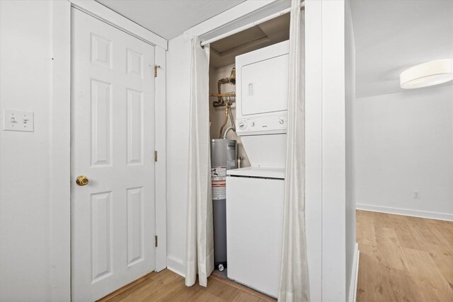 laundry area featuring stacked washing maching and dryer, electric water heater, and light wood-type flooring