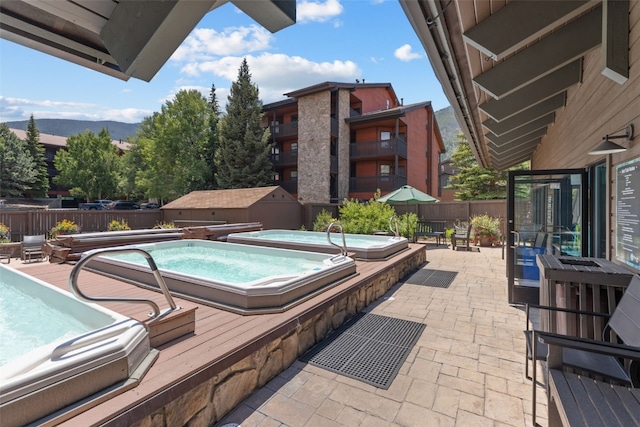 pool with a fenced backyard, a community hot tub, a patio, and a storage unit