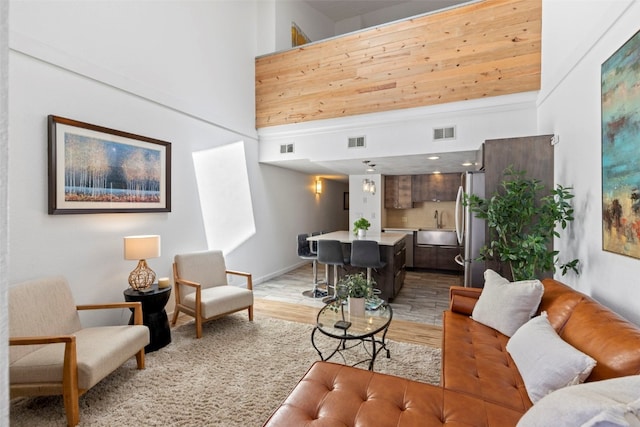 living area with baseboards, light wood finished floors, a towering ceiling, and visible vents