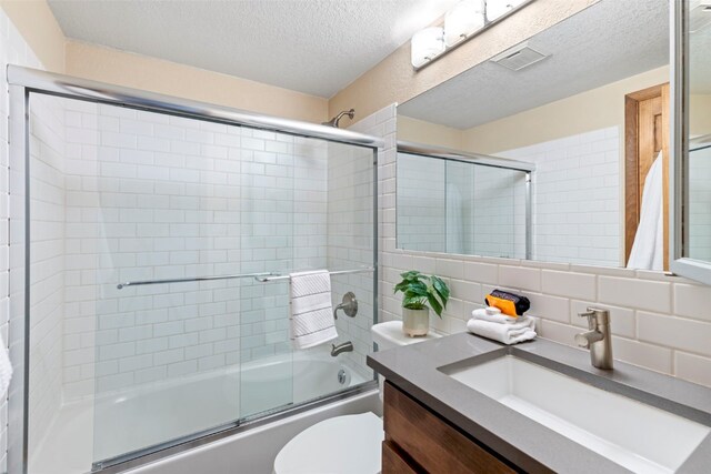 bathroom featuring a textured ceiling, vanity, bath / shower combo with glass door, backsplash, and toilet