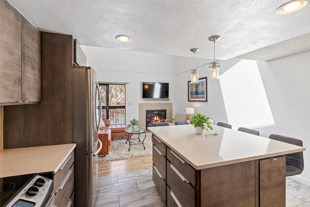 kitchen featuring a textured ceiling, light countertops, electric range oven, a tiled fireplace, and freestanding refrigerator