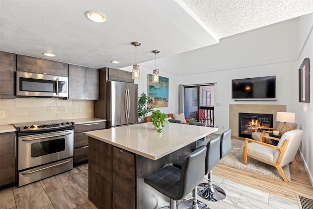 kitchen featuring stainless steel appliances, a kitchen breakfast bar, light countertops, and dark brown cabinetry