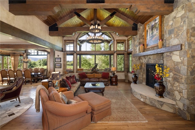 living room featuring a healthy amount of sunlight, a notable chandelier, a stone fireplace, and beamed ceiling