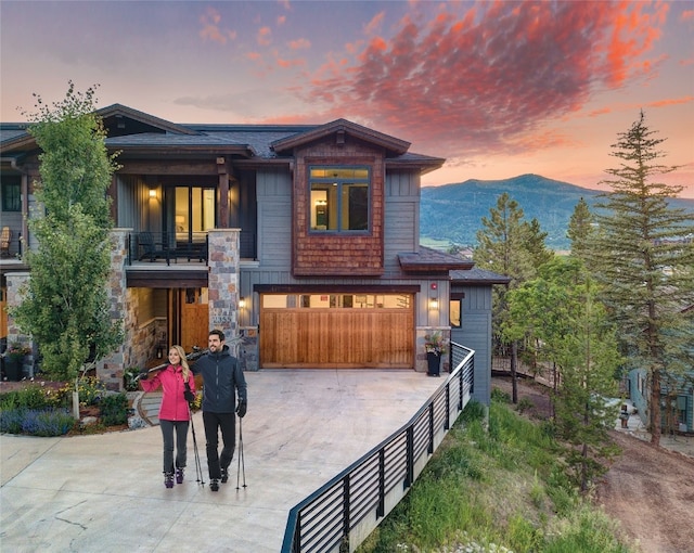 view of front facade with a mountain view, a balcony, a garage, driveway, and stone siding