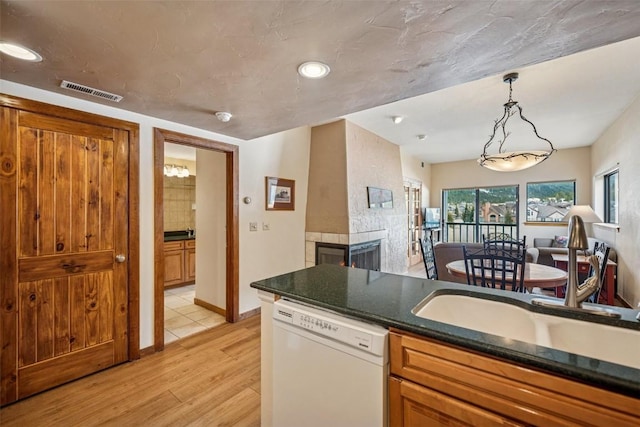 kitchen featuring visible vents, dark countertops, a tile fireplace, dishwasher, and light wood-style floors