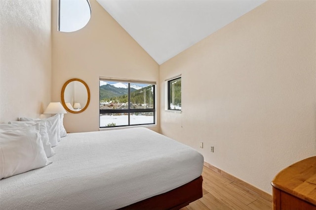 bedroom with high vaulted ceiling, baseboards, a mountain view, and light wood-style flooring