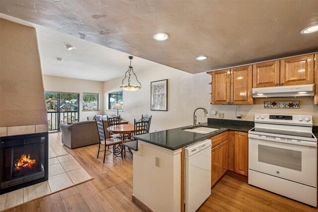 kitchen featuring dark countertops, a sink, white appliances, a peninsula, and under cabinet range hood