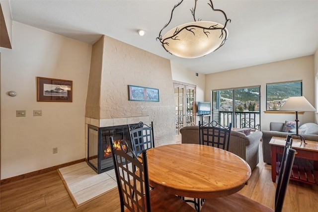 dining space with baseboards, light wood-style flooring, french doors, and a tile fireplace