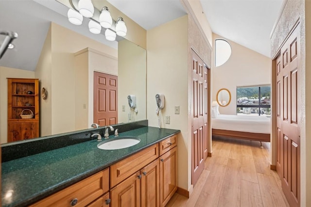 ensuite bathroom with vaulted ceiling, wood finished floors, vanity, baseboards, and ensuite bath