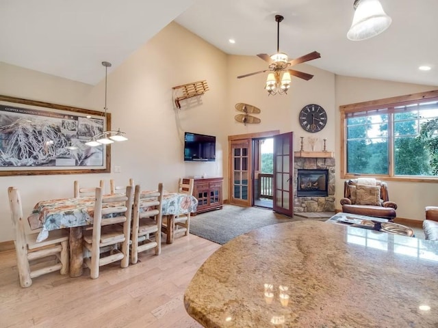 dining room with light wood-style flooring, recessed lighting, a ceiling fan, a stone fireplace, and high vaulted ceiling