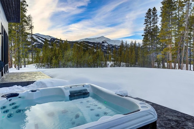 snowy yard with a forest view, a hot tub, and a mountain view