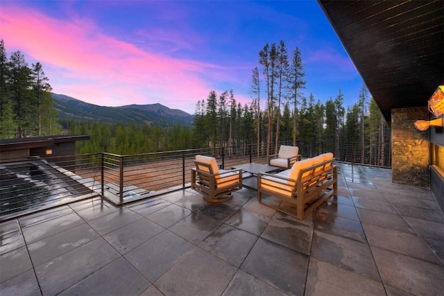 patio terrace at dusk featuring a wooded view, a mountain view, and a balcony