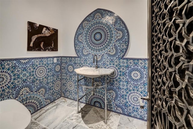 half bathroom with a wainscoted wall, marble finish floor, a sink, and toilet