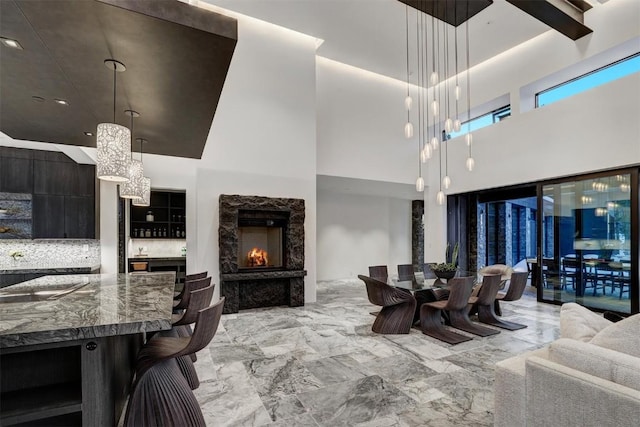 dining space featuring marble finish floor, a high ceiling, a fireplace, and an inviting chandelier