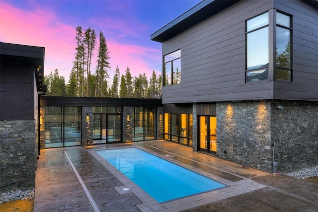 pool at dusk with an outdoor pool and a patio area