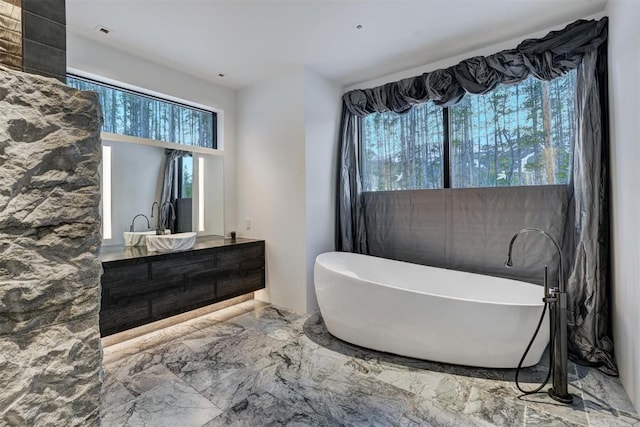 full bathroom with double vanity, a freestanding tub, and marble finish floor
