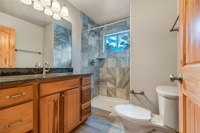bathroom featuring tiled shower, wood finished floors, vanity, and toilet