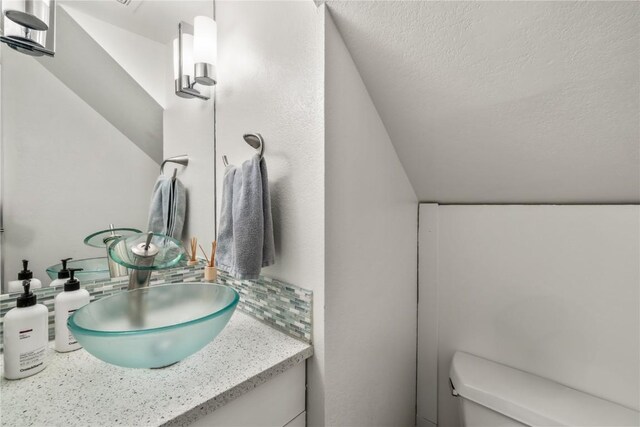 21 Cypress Ct, Steamboat Springs, CO 80487 - half bathroom with toilet, vanity, vaulted ceiling, and a textured ceiling