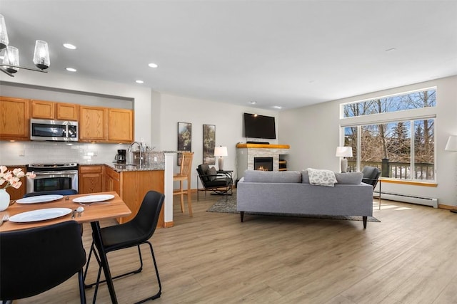 kitchen featuring a warm lit fireplace, stainless steel appliances, light wood-style floors, tasteful backsplash, and baseboard heating