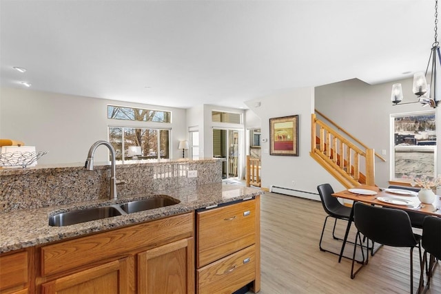 kitchen with a baseboard heating unit, light stone counters, light wood-style flooring, brown cabinetry, and a sink