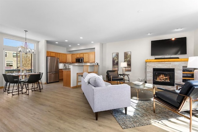 living area with a tiled fireplace, a notable chandelier, recessed lighting, and light wood-type flooring