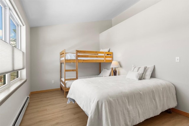 bedroom with a baseboard heating unit, wood finished floors, and baseboards