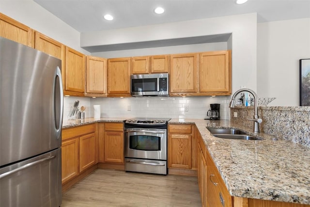 kitchen featuring light wood finished floors, backsplash, appliances with stainless steel finishes, a peninsula, and a sink