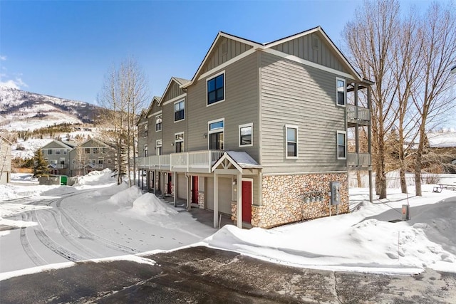 view of snowy exterior featuring stone siding, a garage, board and batten siding, and a balcony