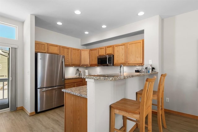 kitchen with light stone countertops, a breakfast bar area, light wood-style flooring, appliances with stainless steel finishes, and a peninsula