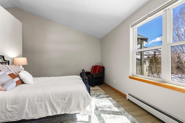 bedroom featuring a baseboard heating unit, lofted ceiling, and wood finished floors