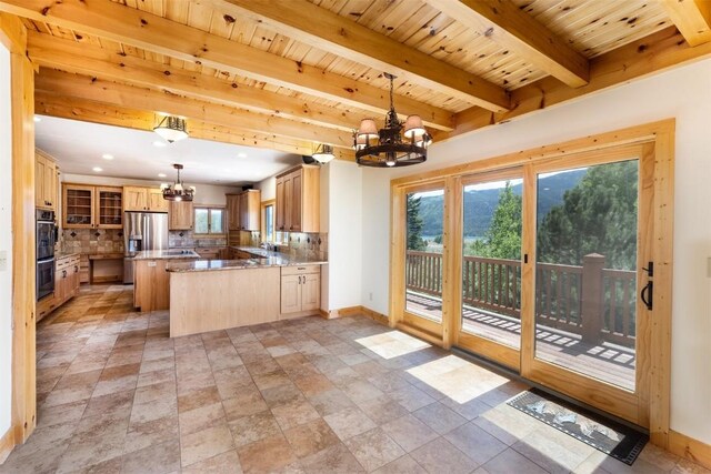 kitchen featuring backsplash, decorative light fixtures, a healthy amount of sunlight, kitchen peninsula, and a chandelier