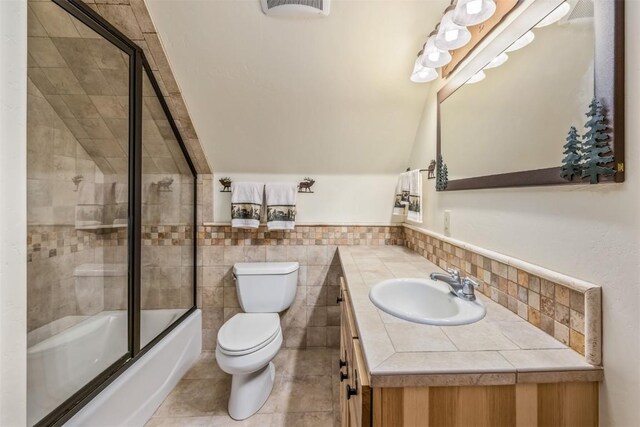 full bathroom with vanity, shower / bath combination with glass door, tile patterned flooring, toilet, and tile walls