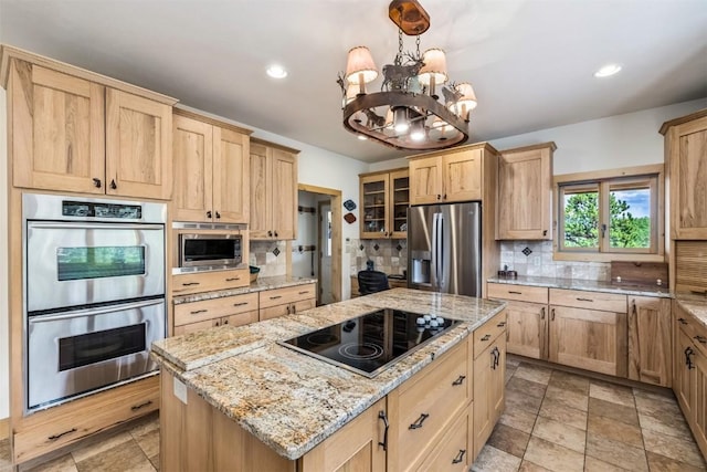 kitchen featuring light stone countertops, a center island, a notable chandelier, decorative backsplash, and appliances with stainless steel finishes