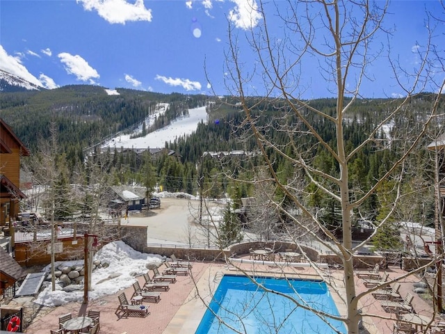snow covered pool with a community pool, a mountain view, a patio, and a wooded view