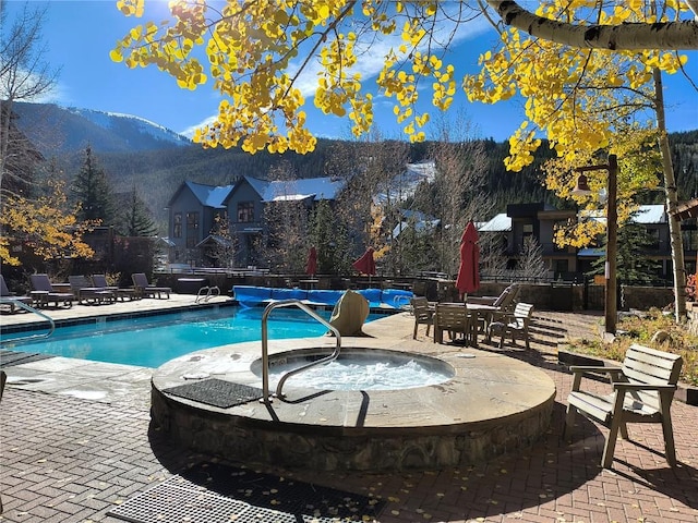 pool with fence, a hot tub, a patio area, and a mountain view
