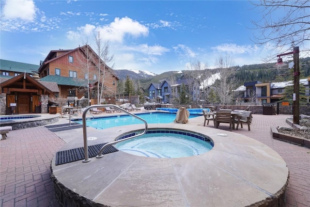 pool with fence, a hot tub, a mountain view, and a patio