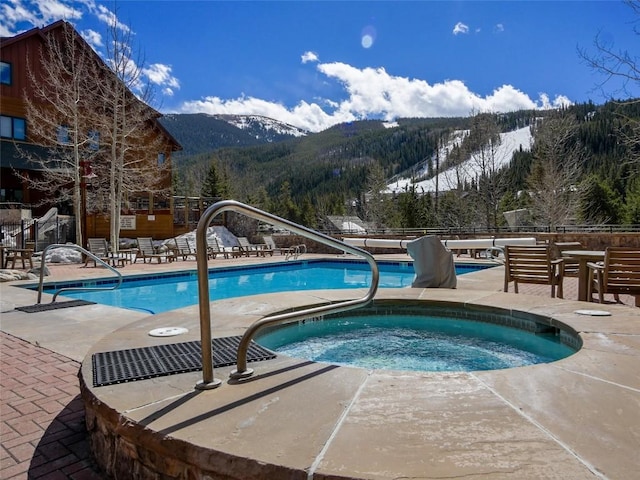 pool with a mountain view, a community hot tub, a patio area, and fence