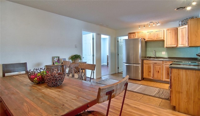 kitchen with light brown cabinetry, dark countertops, visible vents, a sink, and freestanding refrigerator