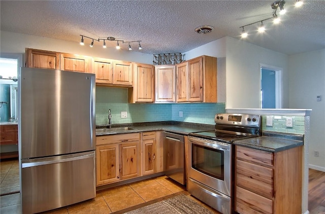 kitchen featuring dark countertops, a sink, decorative backsplash, stainless steel appliances, and rail lighting