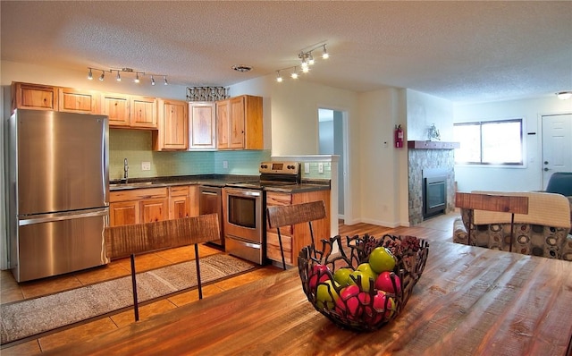 kitchen featuring dark countertops, a sink, decorative backsplash, a textured ceiling, and appliances with stainless steel finishes
