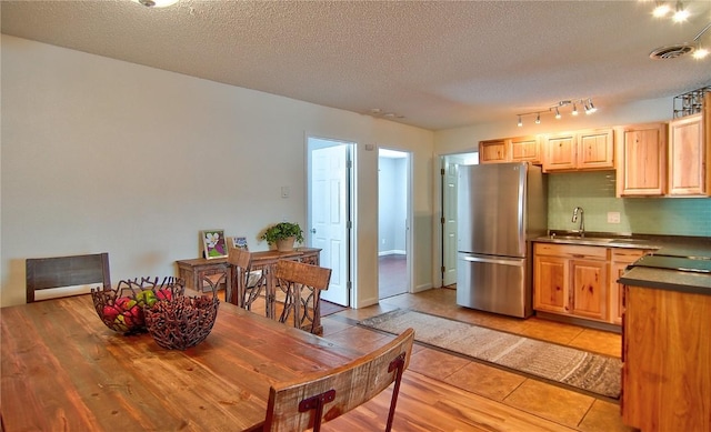 kitchen featuring light brown cabinets, dark countertops, a sink, visible vents, and freestanding refrigerator