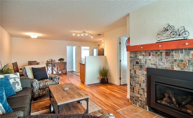 living area with light wood-style flooring, a glass covered fireplace, and a textured ceiling