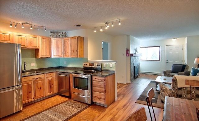 kitchen featuring dark countertops, a sink, a baseboard heating unit, stainless steel appliances, and rail lighting