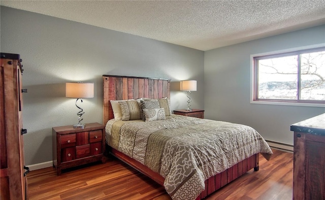 bedroom featuring a baseboard heating unit, wood finished floors, a textured ceiling, and baseboards