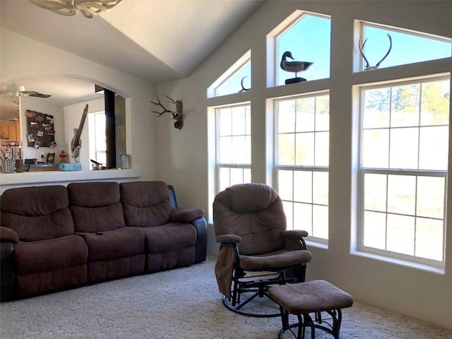 carpeted living area featuring arched walkways, vaulted ceiling, and plenty of natural light