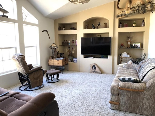carpeted living area with built in shelves and lofted ceiling