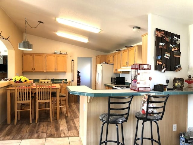 kitchen featuring lofted ceiling, a peninsula, tile counters, and a kitchen breakfast bar