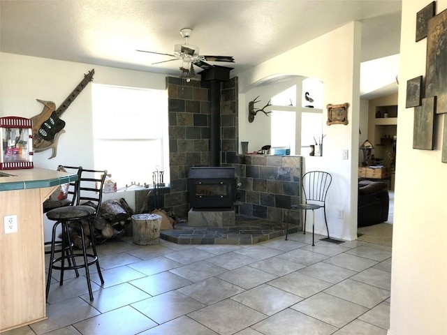 living area with a wood stove, a ceiling fan, and light tile patterned floors