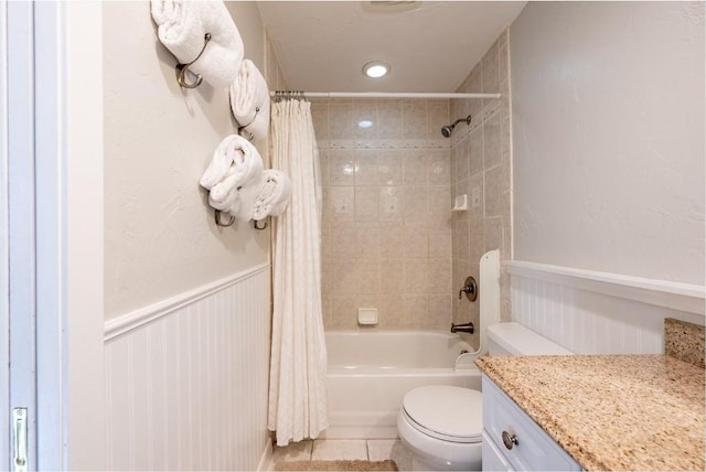 full bath featuring a wainscoted wall, tile patterned floors, toilet, vanity, and shower / bath combo